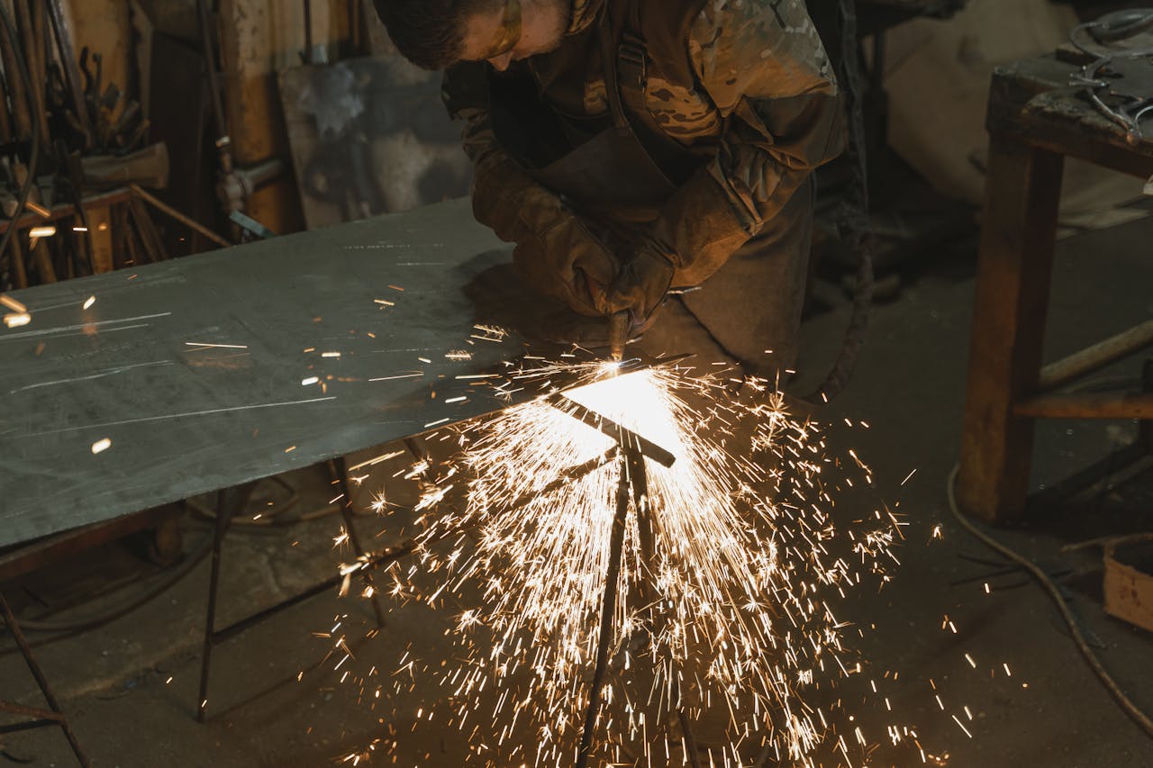 gallery-2 A professional welder cutting metal in an industrial workshop with bright sparks flying around.