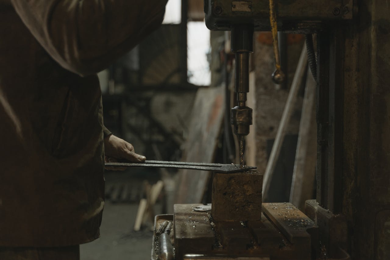 A craftsman uses a drill press indoors, showcasing industrial craftsmanship and precision.